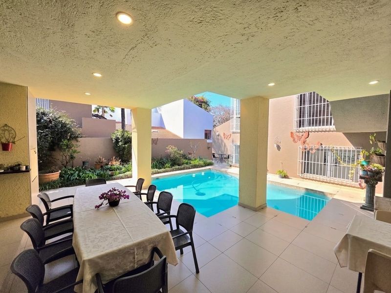 Covered outdoor patio area featuring tiled flooring and recessed lighting, overlooking a private swimming pool and landscaped garden.