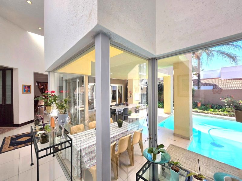 Bright open-plan living area featuring floor-to-ceiling glass walls that provide seamless views of the outdoor swimming pool and patio area.