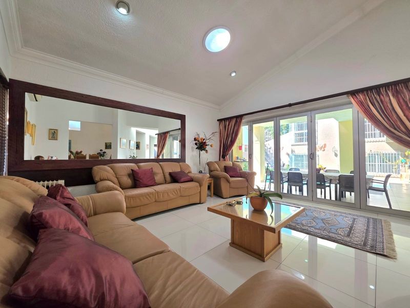 Spacious living room featuring large sliding glass doors leading to a patio, tiled flooring, recessed lighting, and a large decorative wall mirror.