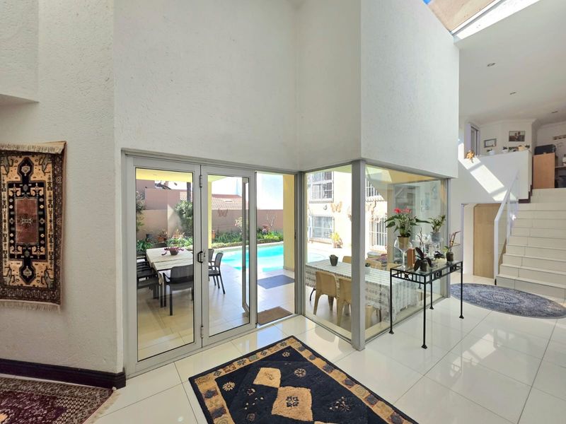 Bright living area featuring double-height ceilings, large glass corner windows, and direct access to the outdoor pool area.