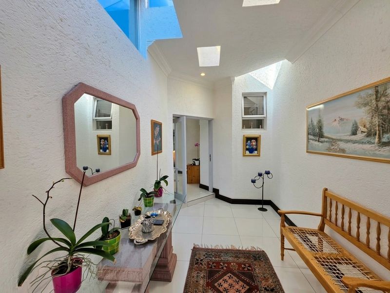 A bright, spacious hallway featuring tiled flooring, textured walls, and multiple skylights that provide ample natural light throughout the entrance area.