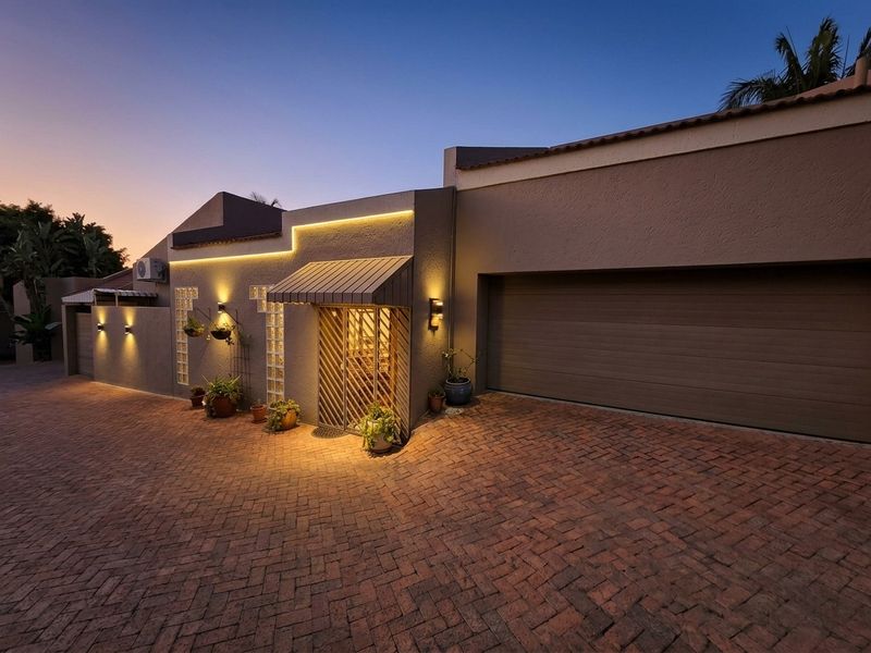 Front elevation of the property featuring a brick paved driveway, integrated garage, and modern exterior lighting with a secure entrance gate.