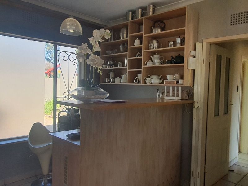 A home bar area featuring a built-in wooden counter and open shelving, with large windows and tiled flooring.