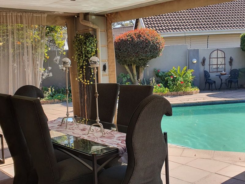 A covered outdoor patio area overlooking a private swimming pool and landscaped garden, providing a seamless transition for outdoor dining and entertainment.