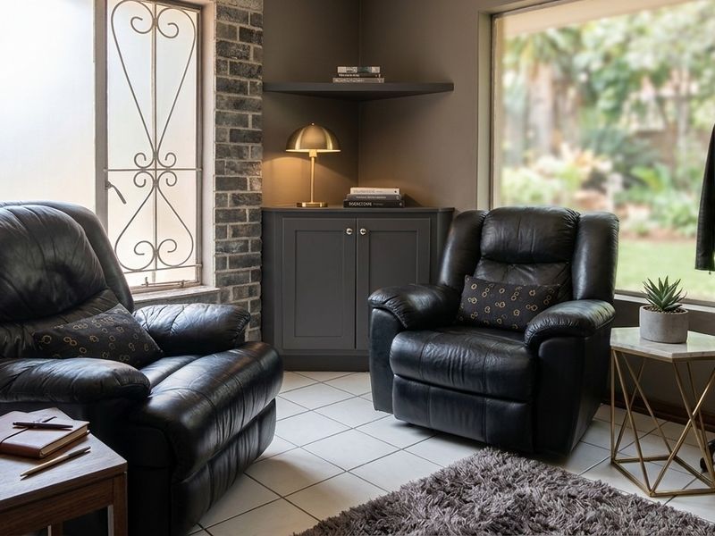 A cozy living area featuring exposed brick accents, built-in corner cabinetry, and large windows with security bars overlooking the garden.