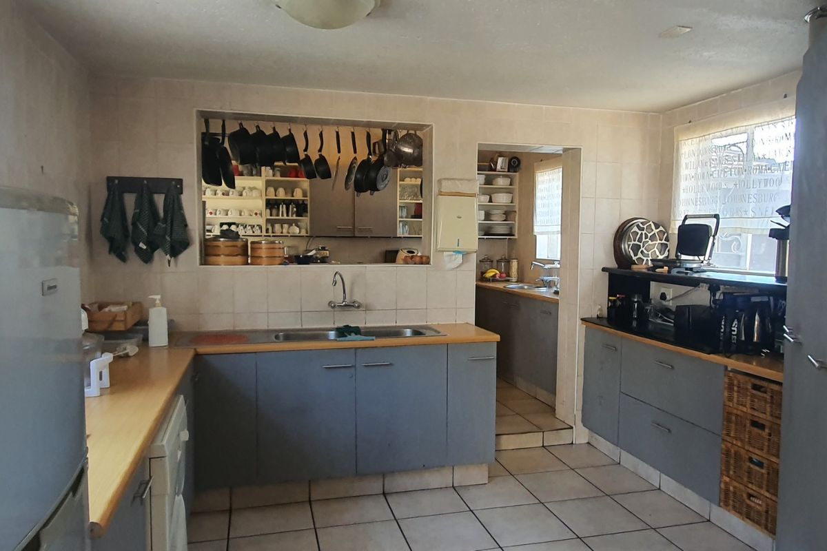 A functional kitchen featuring tiled flooring, laminate countertops, double bowl sink, and a convenient pass-through window connecting to the adjacent scullery area.