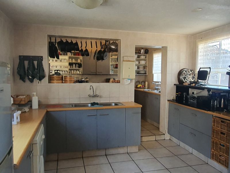 A functional kitchen featuring tiled flooring, laminate countertops, double bowl sink, and a convenient pass-through window connecting to the adjacent scullery area.