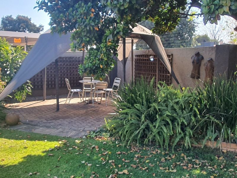 A landscaped garden featuring a paved patio area, established trees, and a boundary wall with integrated trellis panels and electric fencing.