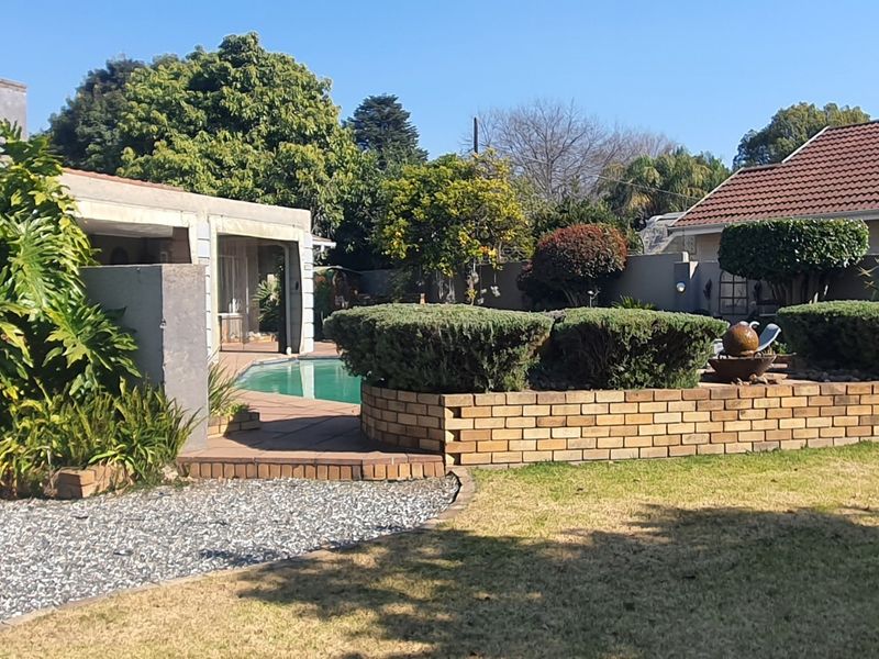 A well-maintained rear garden featuring a swimming pool, timber decking, and a decorative brick retaining wall with established landscaping.