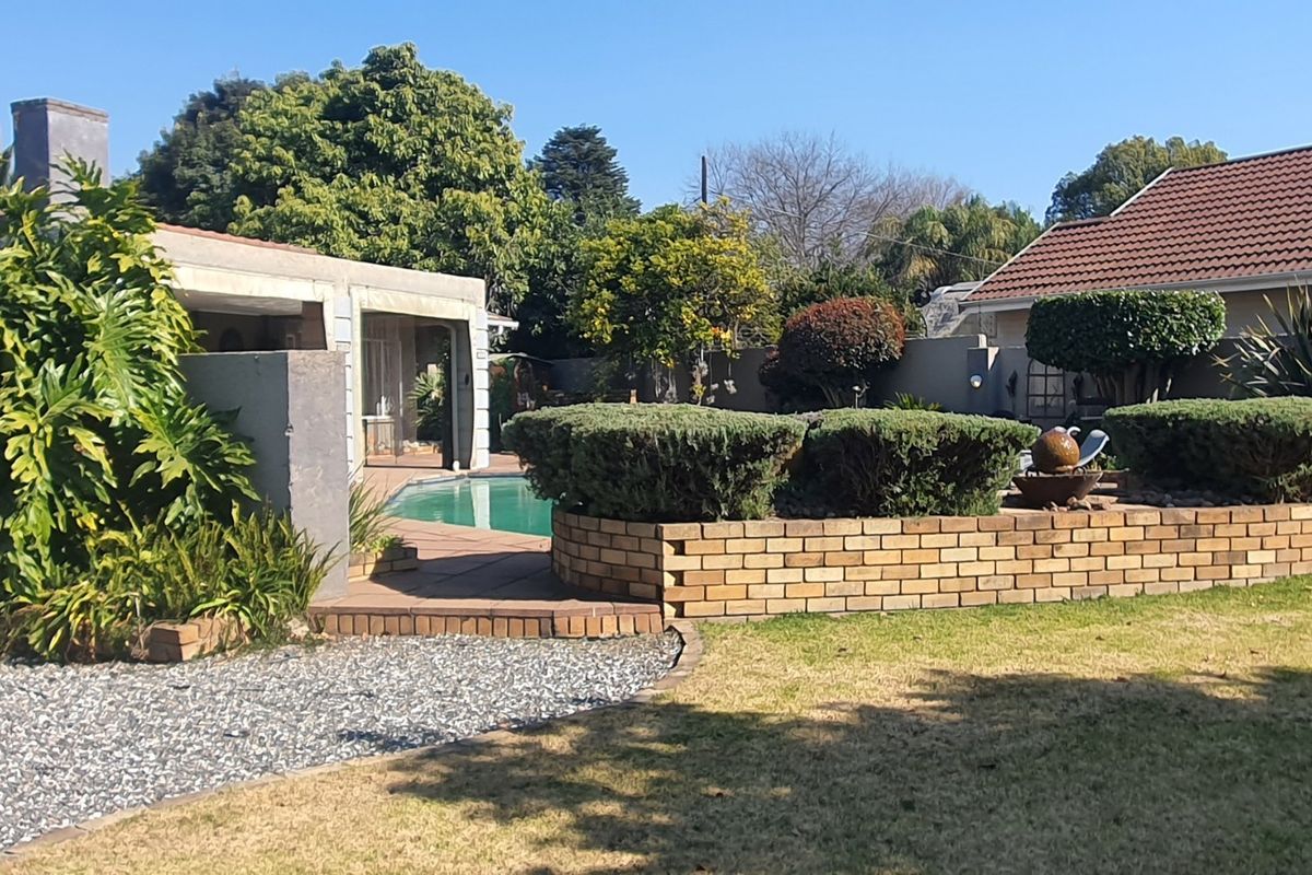 A well-maintained rear garden featuring a swimming pool, timber decking, and a decorative brick retaining wall with established landscaping.