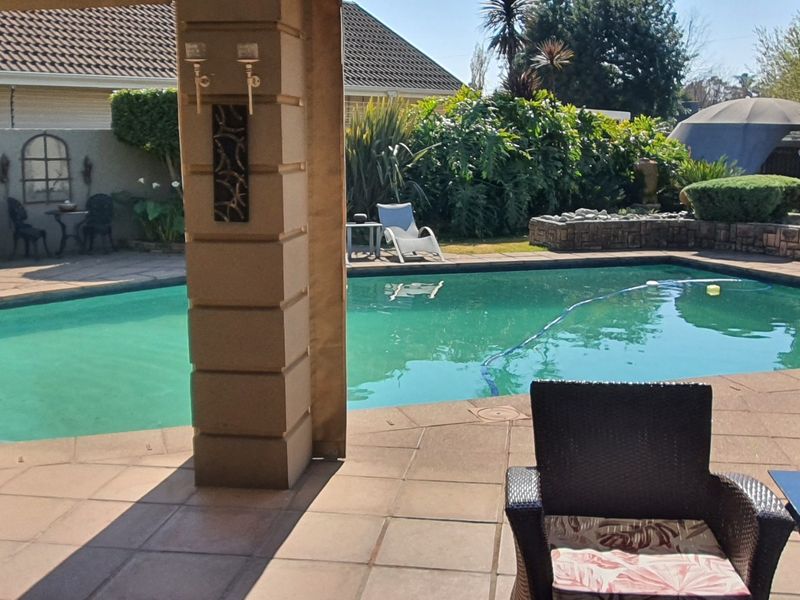 A covered patio area overlooking a swimming pool with stone retaining walls and established garden landscaping.