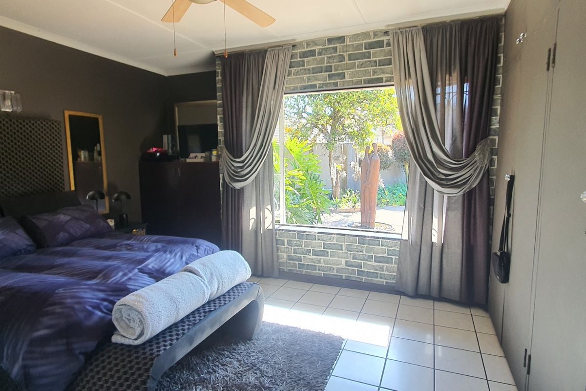Spacious bedroom featuring a brick accent wall, built-in cupboards, tiled flooring, and a large window overlooking the garden.