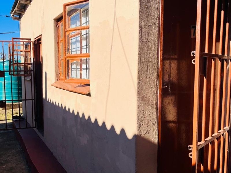 Exterior view of the property entrance featuring a security gate, timber window frames, and a corrugated metal roof.