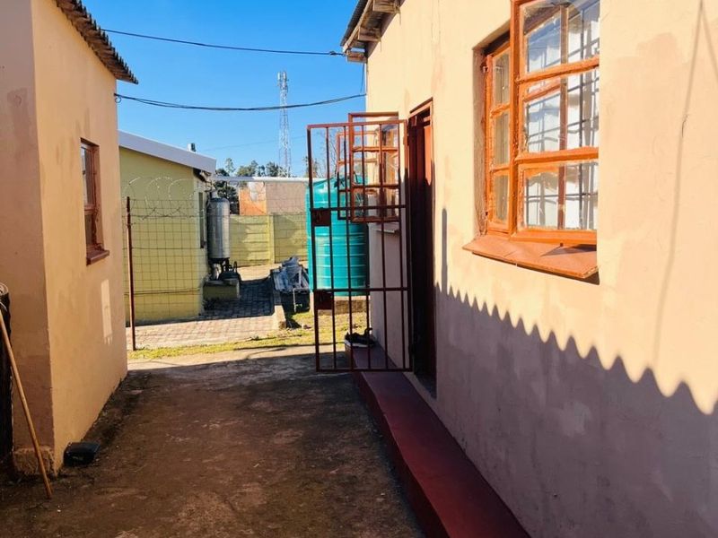 A narrow exterior side passage between two structures featuring concrete paving, security gates, and a water tank in the rear yard area.