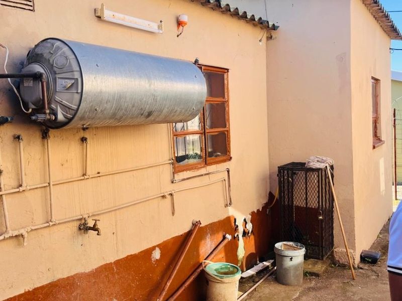 Rear exterior view of the property showing an external geyser installation, exposed plumbing, and weathered wall finishes.