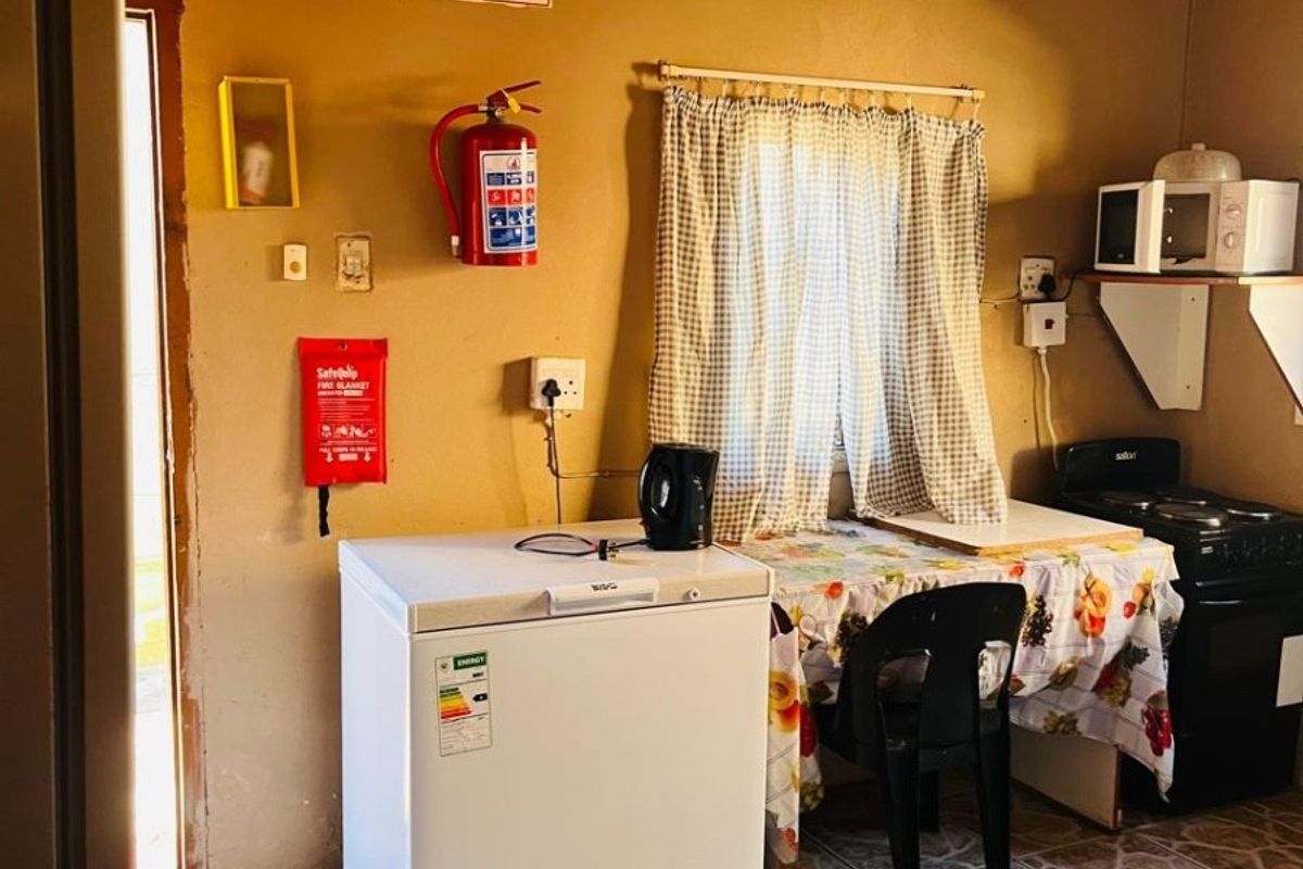 A compact kitchen area featuring tiled flooring, a timber ceiling, and a freestanding stove, with basic wall-mounted fire safety equipment.