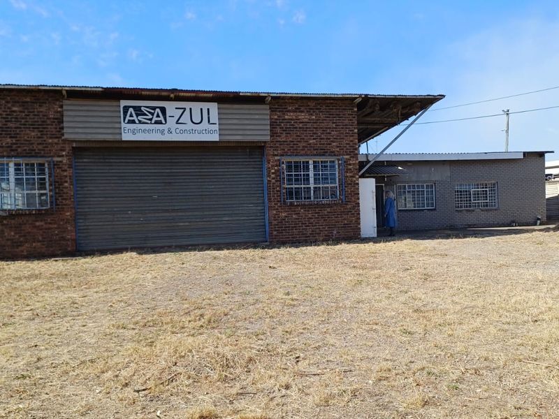 Industrial property featuring a brick facade, large roller shutter door, and security-barred windows, situated on a large open plot.