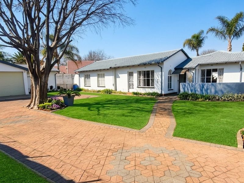 Well-maintained front exterior featuring a paved driveway, double garage, and a neatly landscaped garden with established trees.