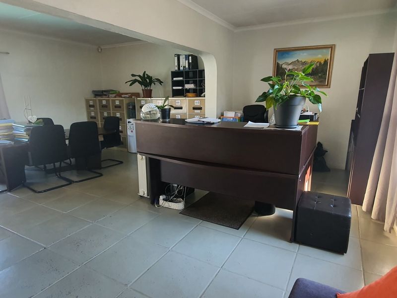 A functional office space featuring tiled flooring, an open-plan layout with an archway, and a wall-mounted radiator.
