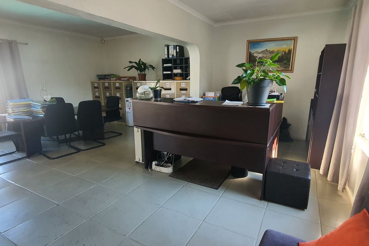 A functional office space featuring tiled flooring, an open-plan layout with an archway, and a wall-mounted radiator.