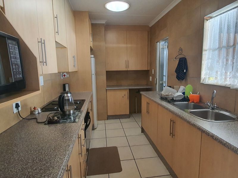 A functional galley-style kitchen featuring light wood-finish cabinetry, granite-look laminate countertops, a double stainless steel sink, and built-in appliances.