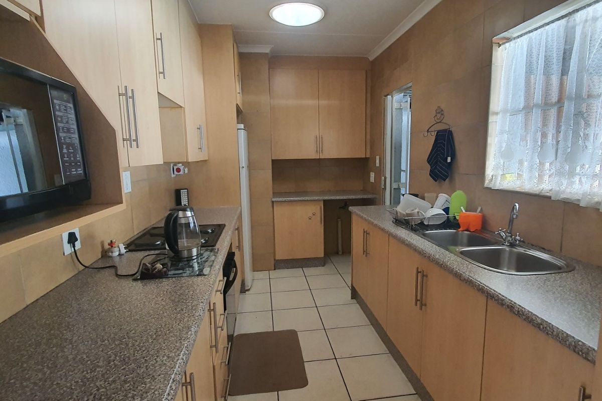 A functional galley-style kitchen featuring light wood-finish cabinetry, granite-look laminate countertops, a double stainless steel sink, and built-in appliances.