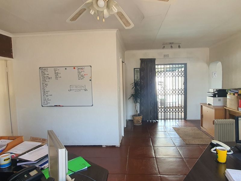 A living area featuring tiled flooring, an exposed brick feature wall, and a security gate leading to the exterior.