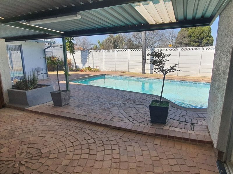 A covered outdoor patio area featuring paved flooring, overlooking a private swimming pool and enclosed by a perimeter wall.