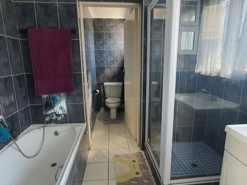 A functional bathroom featuring a bathtub, separate shower enclosure, vanity basin, and toilet with dark blue wall tiling.