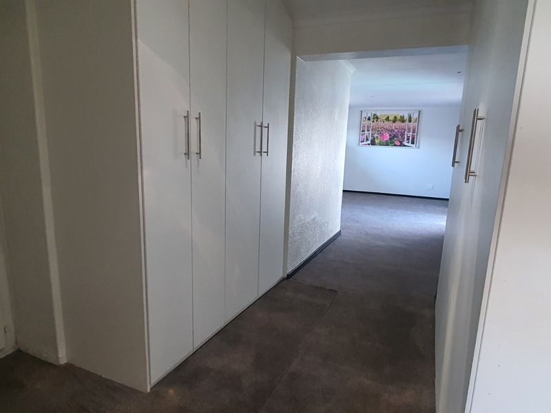 A hallway featuring built-in storage cupboards and carpeted flooring, leading into an adjacent living space.