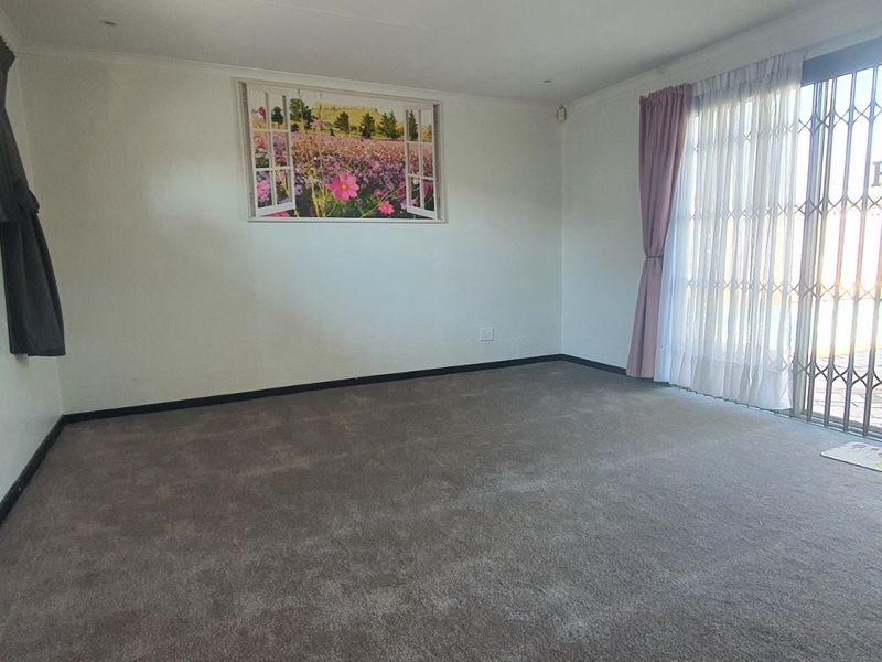 A spacious, empty living room featuring neutral carpeting, recessed lighting, and a sliding glass door with a security gate leading to the exterior.
