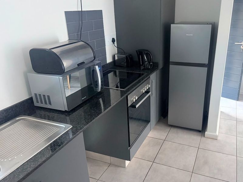 A modern, compact kitchen featuring dark grey cabinetry, granite countertops, a built-in oven with electric hob, and neutral tiled flooring.