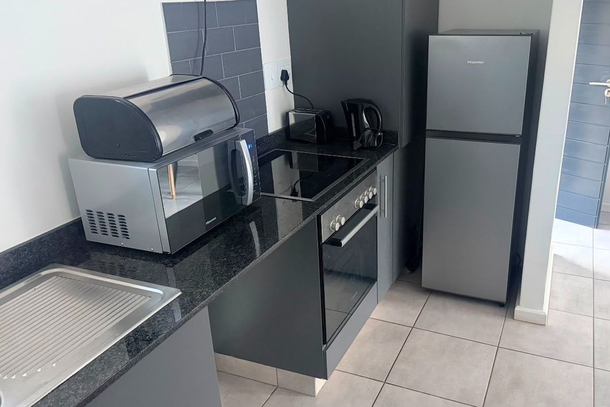 A modern, compact kitchen featuring dark grey cabinetry, granite countertops, a built-in oven with electric hob, and neutral tiled flooring.