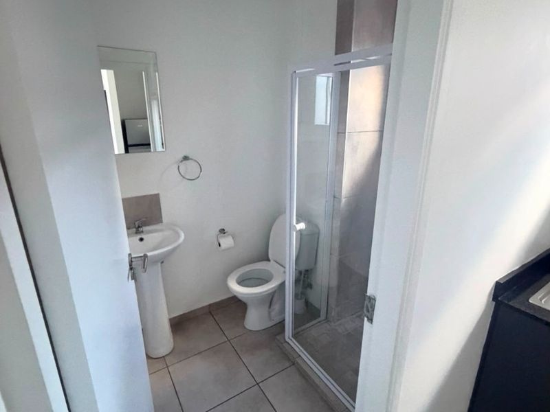 A compact bathroom featuring a pedestal basin, toilet, and a glass-enclosed shower with neutral floor tiling.