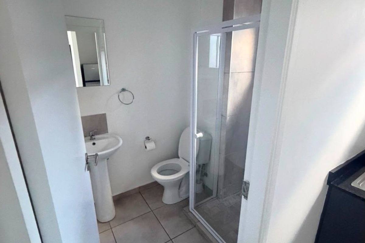 A compact bathroom featuring a pedestal basin, toilet, and a glass-enclosed shower with neutral floor tiling.