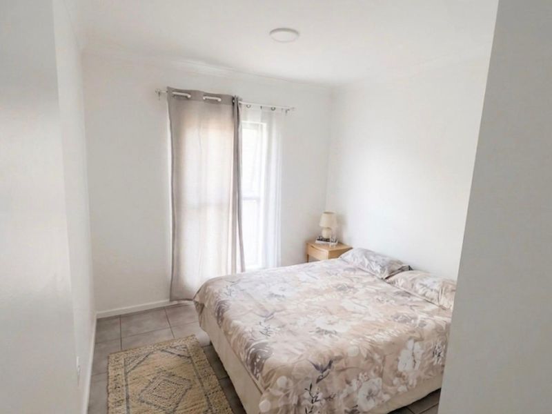 A simple bedroom featuring neutral tiled flooring and a window with curtain fixtures, providing a clean and functional living space.