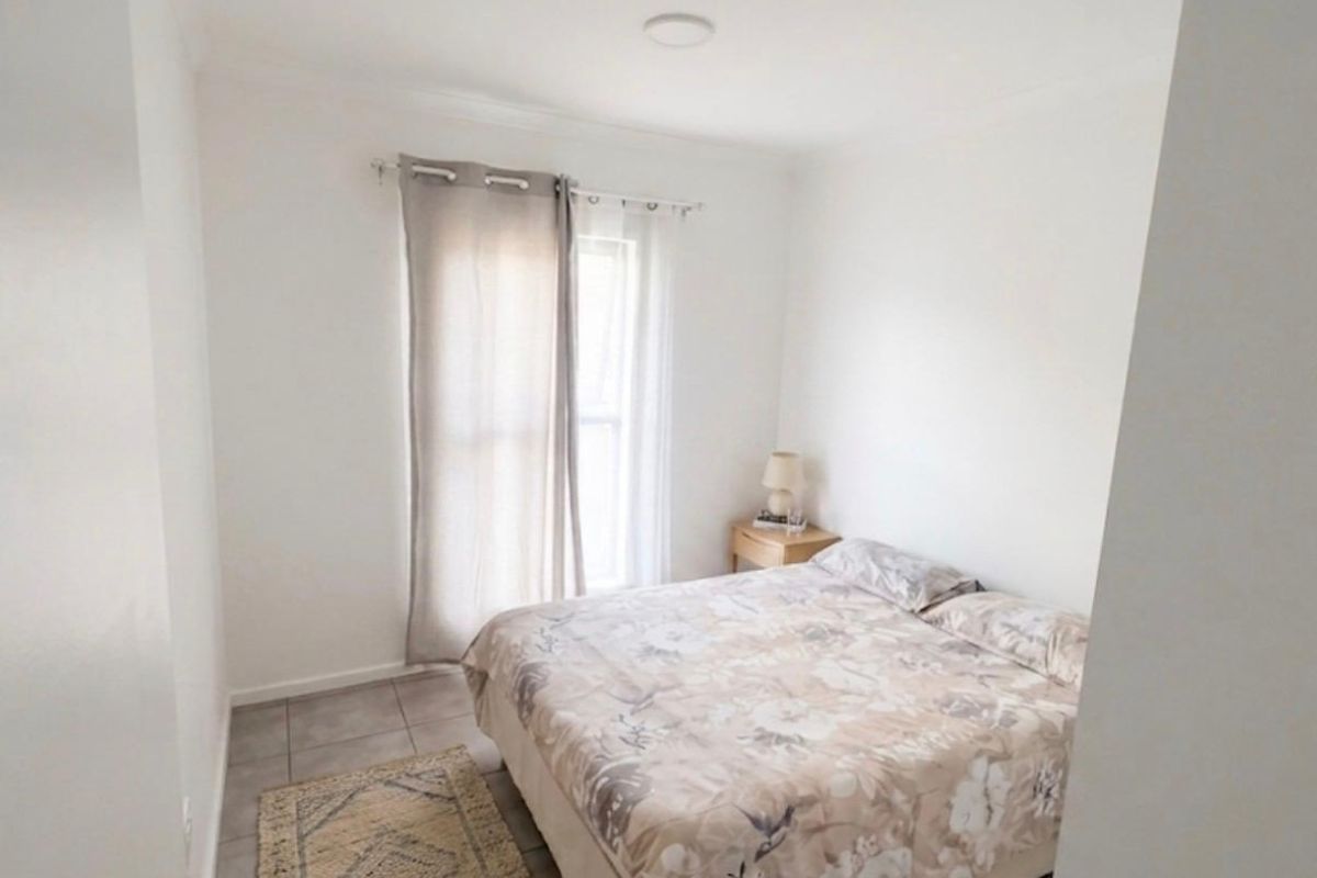 A simple bedroom featuring neutral tiled flooring and a window with curtain fixtures, providing a clean and functional living space.