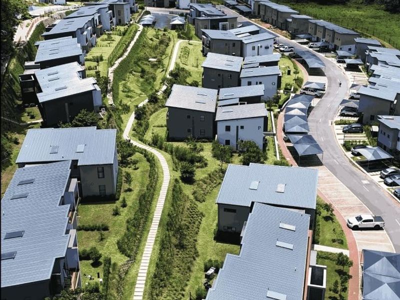 An aerial view of a modern residential apartment complex featuring multiple buildings with metal roofs, paved pathways, and covered parking areas.