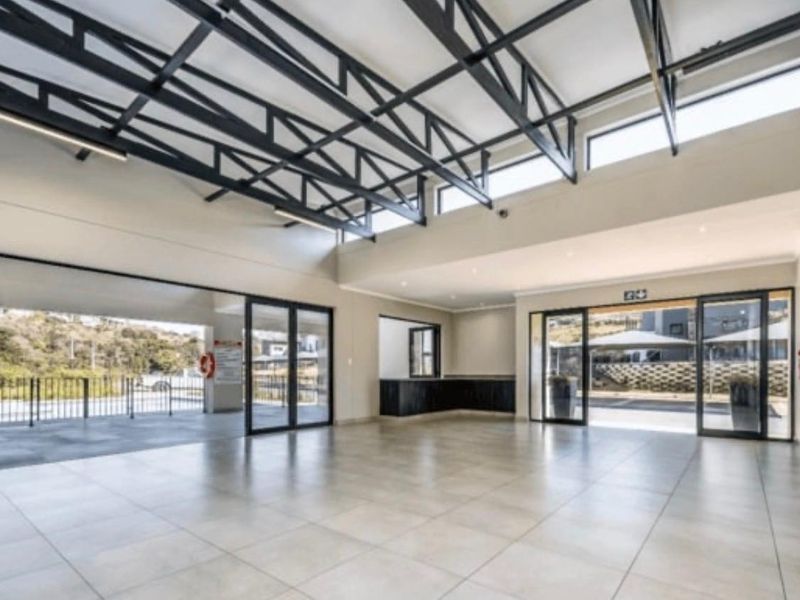A spacious, modern clubhouse area featuring high ceilings with exposed steel trusses, large aluminium sliding doors, and neutral tiled flooring.