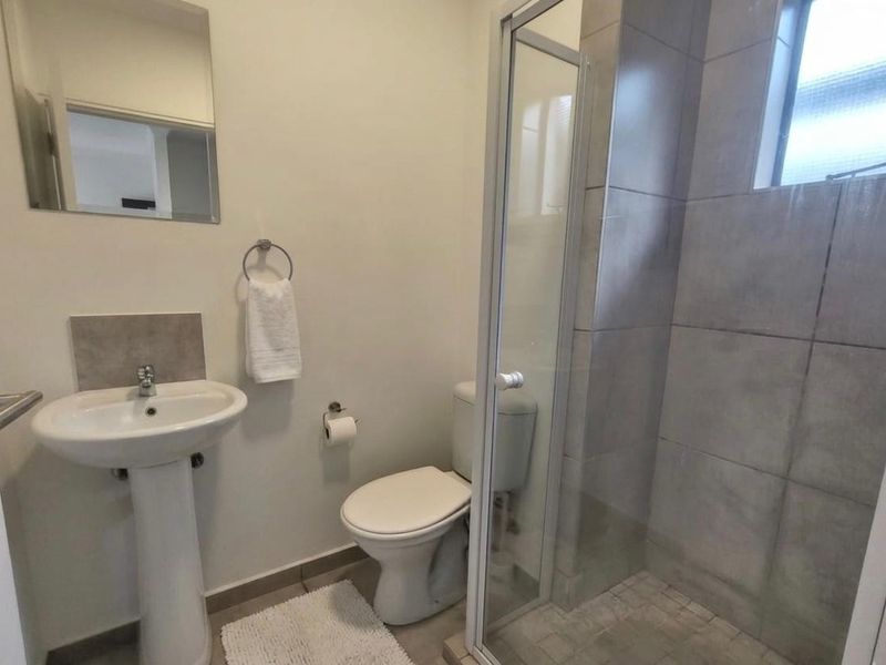 A functional bathroom featuring a pedestal basin, a toilet, and a glass-enclosed shower with neutral wall tiling.