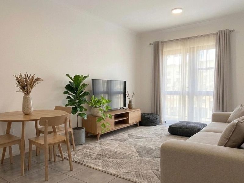 A bright open-plan living and dining area featuring neutral tiled flooring and a large sliding glass door providing access to the balcony.