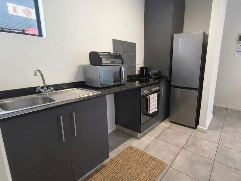 A compact kitchen featuring dark grey cabinetry, granite countertops, a stainless steel sink, and built-in oven with hob.