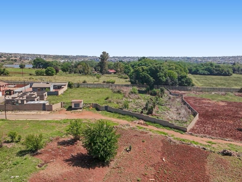Aerial view of a large, undeveloped commercial plot featuring perimeter walling and surrounding natural landscape with nearby residential structures.