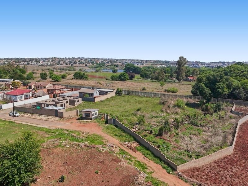 Aerial view of a large, undeveloped commercial plot featuring perimeter walling and boundary fencing, situated in a developing suburban area.
