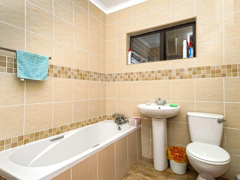 A functional bathroom featuring a pedestal basin, bathtub, and toilet with neutral wall and floor tiling.
