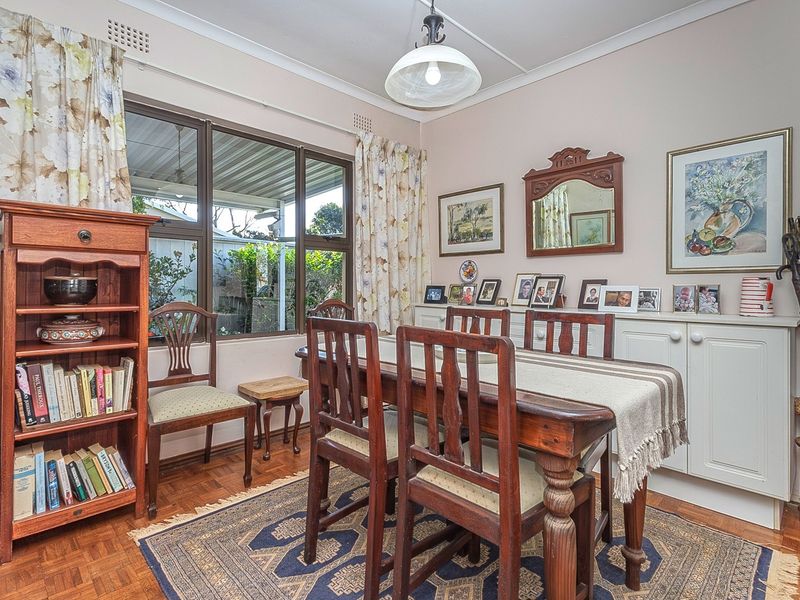 A dining room featuring classic parquet flooring, built-in storage cabinetry, and a large window providing natural light.