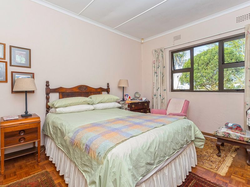 A bedroom featuring parquet flooring, large aluminium-framed windows, and classic cornice detailing, offering a functional space with potential for modern updates.