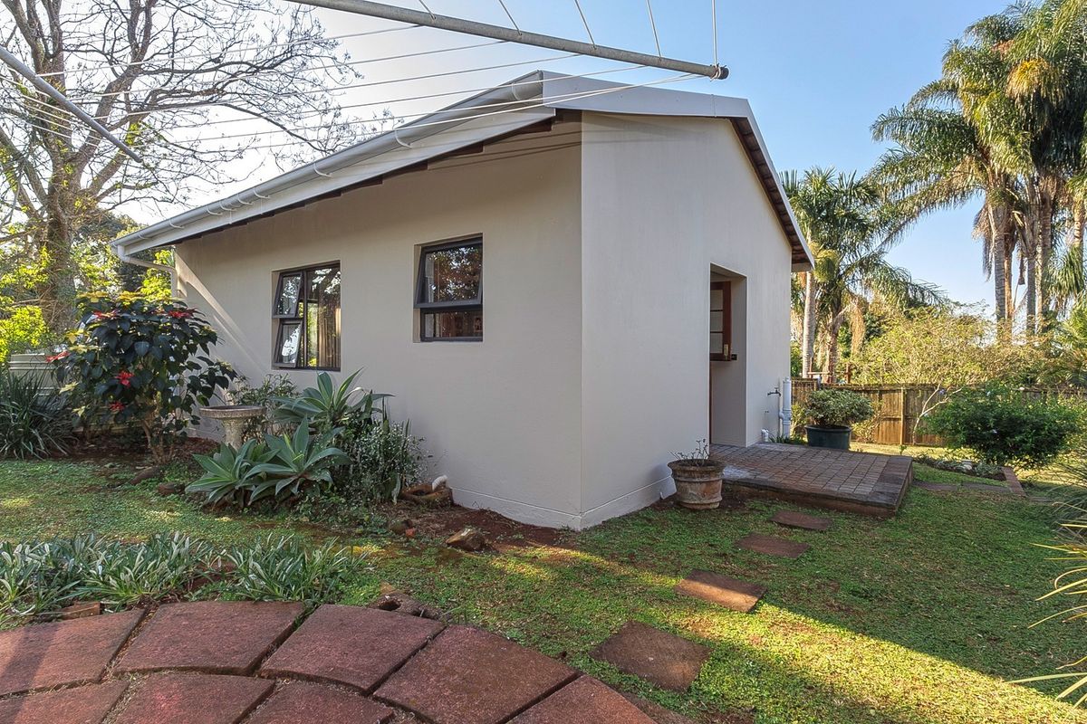 A well-maintained rear exterior view of the property featuring a paved patio area, landscaped garden, and modern aluminium window frames.