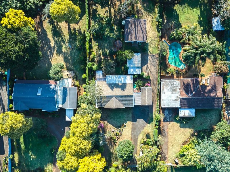 Aerial view of the residential property showing the main dwelling, surrounding landscaped gardens, driveway, and a swimming pool.
