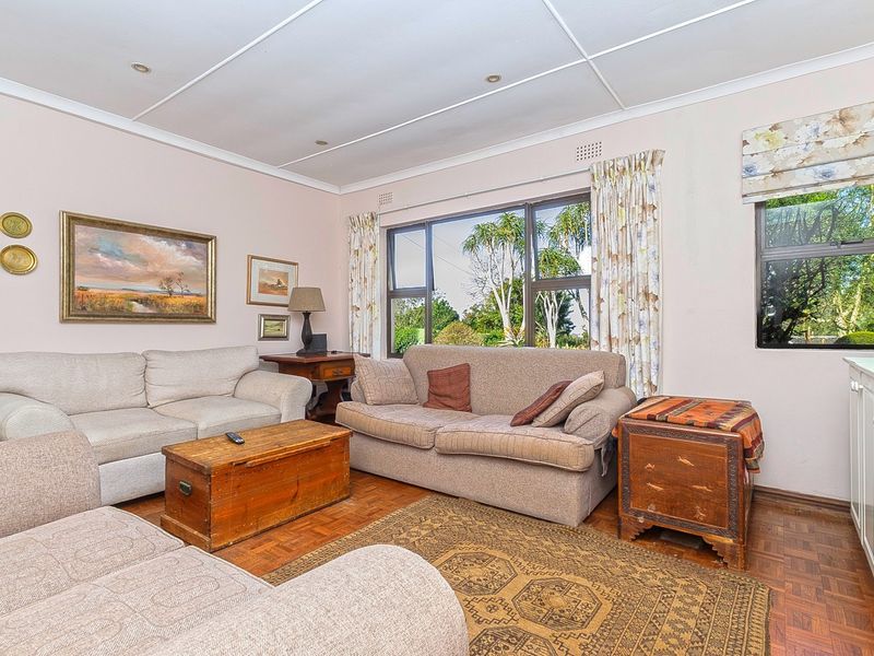 A comfortable living room featuring classic parquet flooring, recessed lighting, and large windows that provide natural light and garden views.